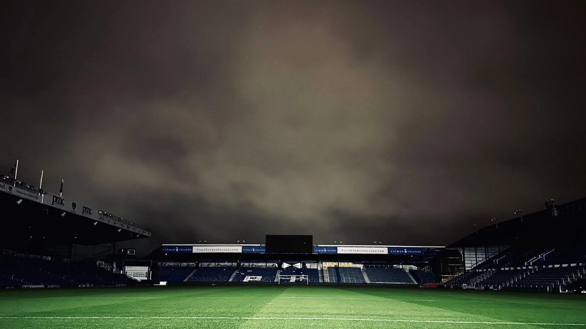 Football stadium at night, dark clouds above, floodlights illuminate the pitch.