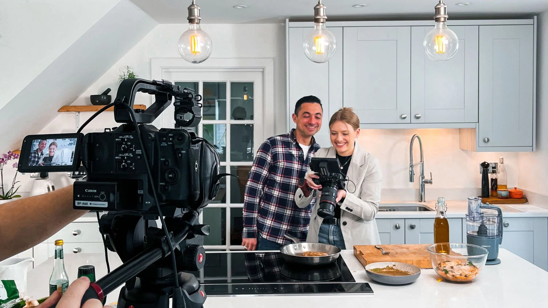 Video camera films smiling duo cooking in a modern kitchen.