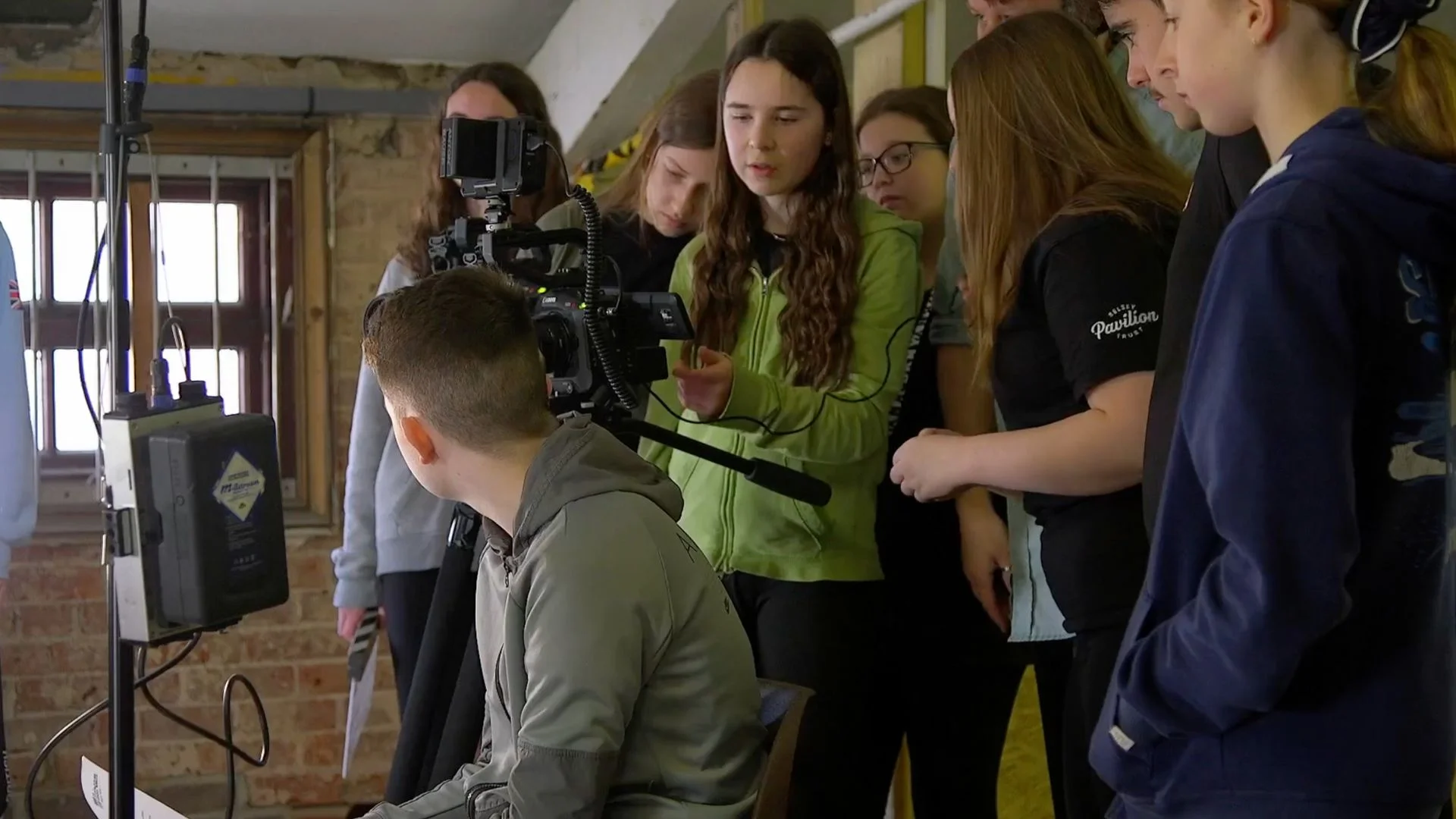 Students intently watch a camera and monitor setup, learning film production.