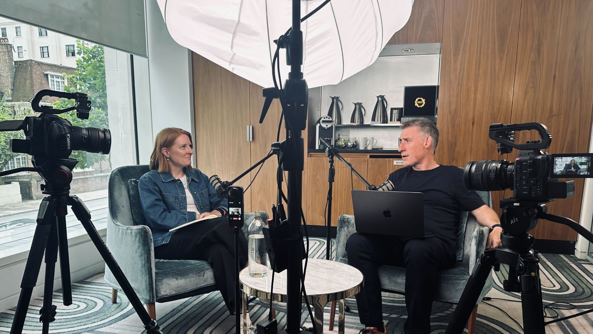 Two people sat in chairs talking to each other and recording a podcast