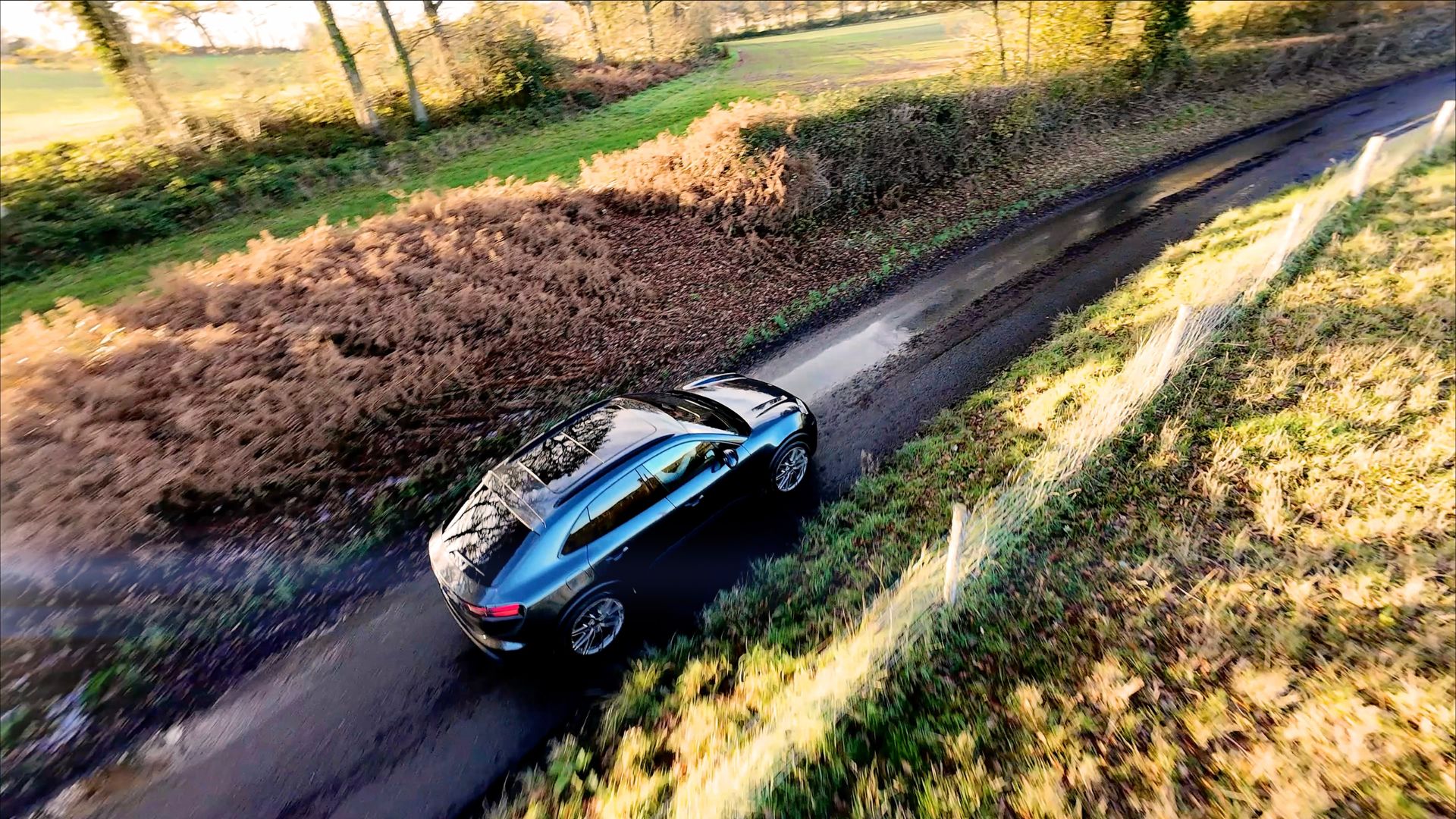 fpv drone still of a porsche driving along a country lane 