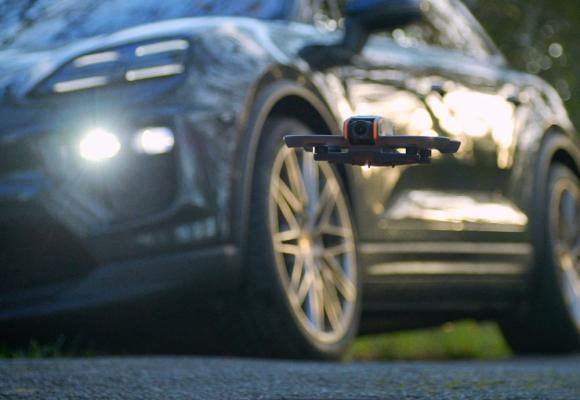 close up photography of a hovering fpv drone with a porsche in the background