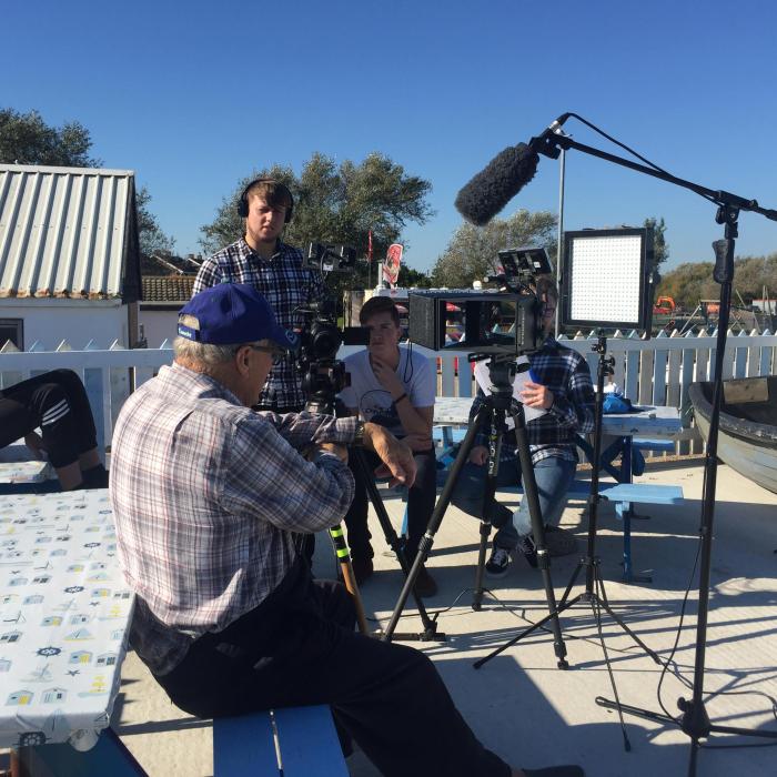 Fisherman sitting on the quay side being interviewed by student filmmakers