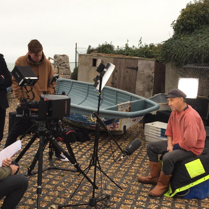 Fisherman sitting on the quay side being interviewed by student filmmakers