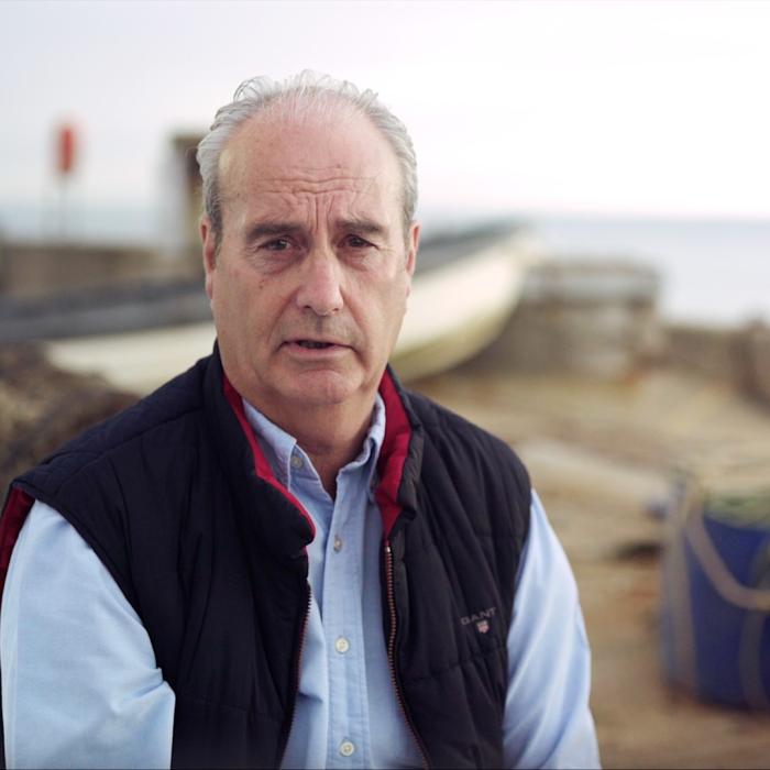 Fisherman sat on the quay side next to lobster pots