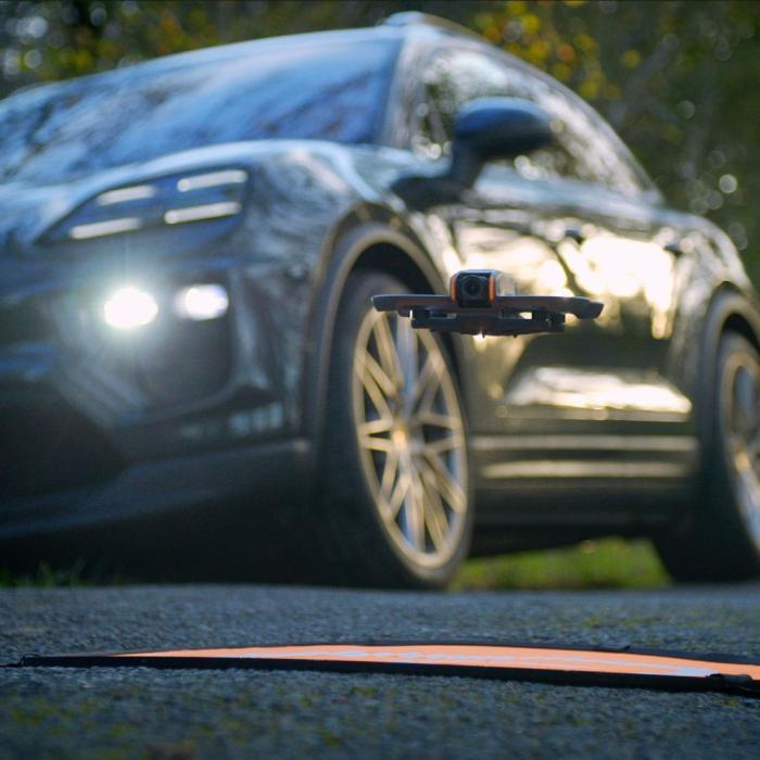close up photography of a hovering fpv drone with a porsche in the background