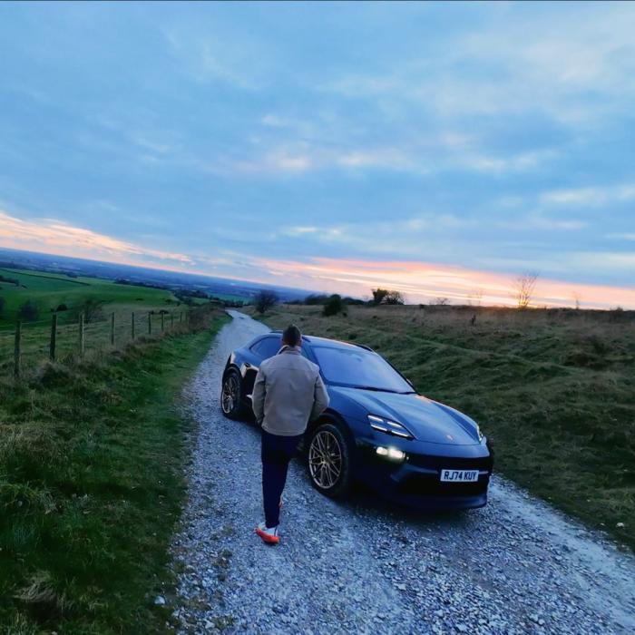 drone photography of someone walking up to a porsche parked on a country road