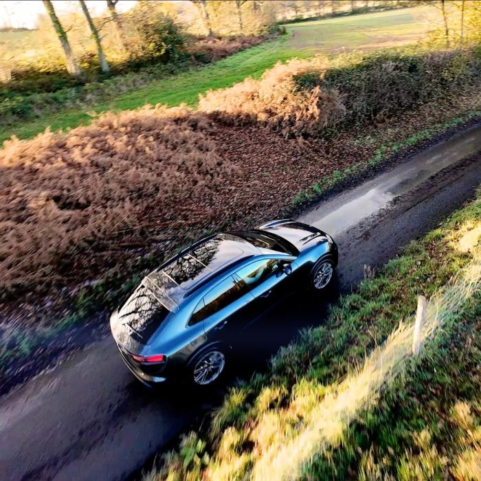 drone photography of a porsche driving along a country lane