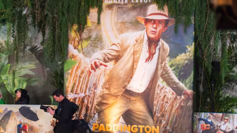 Large Paddington film poster: adventurer in a hat, jungle foliage. People in the foreground.