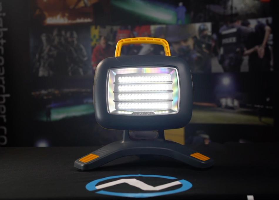 Bright, portable LED work light with dark grey housing and orange handle on a dark surface.