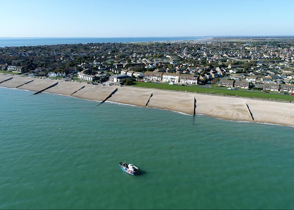 Aerial view of a British seaside town with a beach, groynes, and a boat on the turquoise sea.
