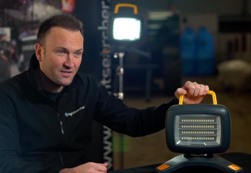 Man holding a portable LED work light with a yellow handle, demonstrating it.