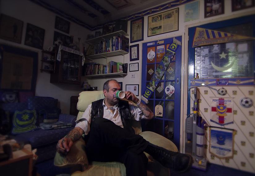 Football fan with tattoos sitting in an arm chair drinking tea