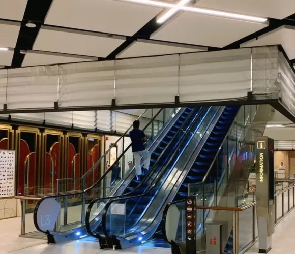 Person on a brightly lit escalator in a modern, spacious building.