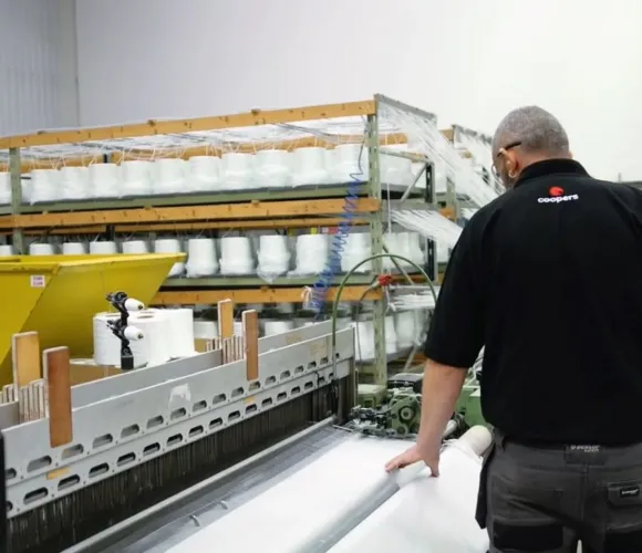 Worker in a factory inspecting white material on a large production machine.