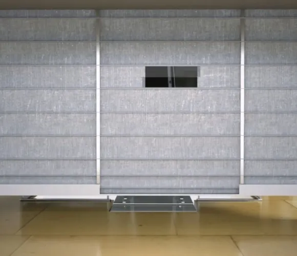 Modern minimalist room with grey horizontal blinds, wooden floor, and two small dark screens.