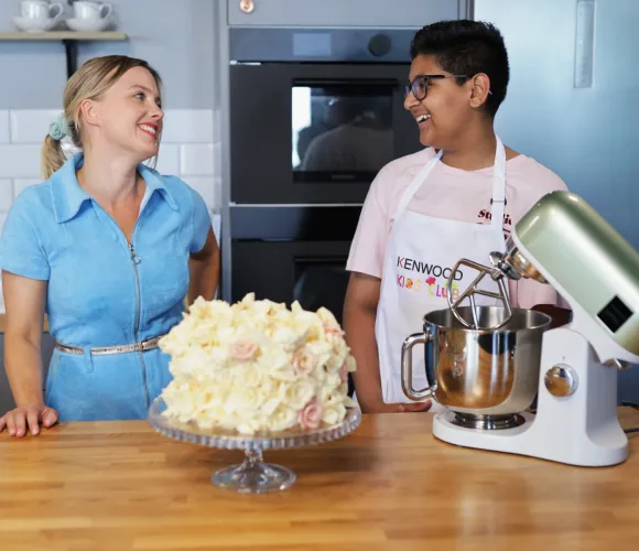 2 people standing in kitchen with cake and mixer