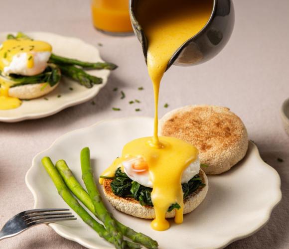 Sauce being poured onto a poached egg and muffin
