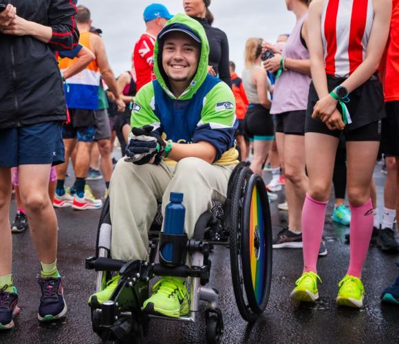 Someone in a wheelchair smiling at the camera surrounded by people in sportswear