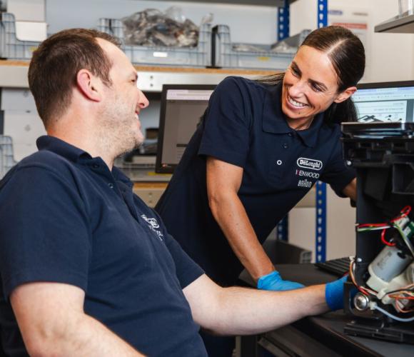 Two De'Longhi employees working on a coffee machine and smiling at each other