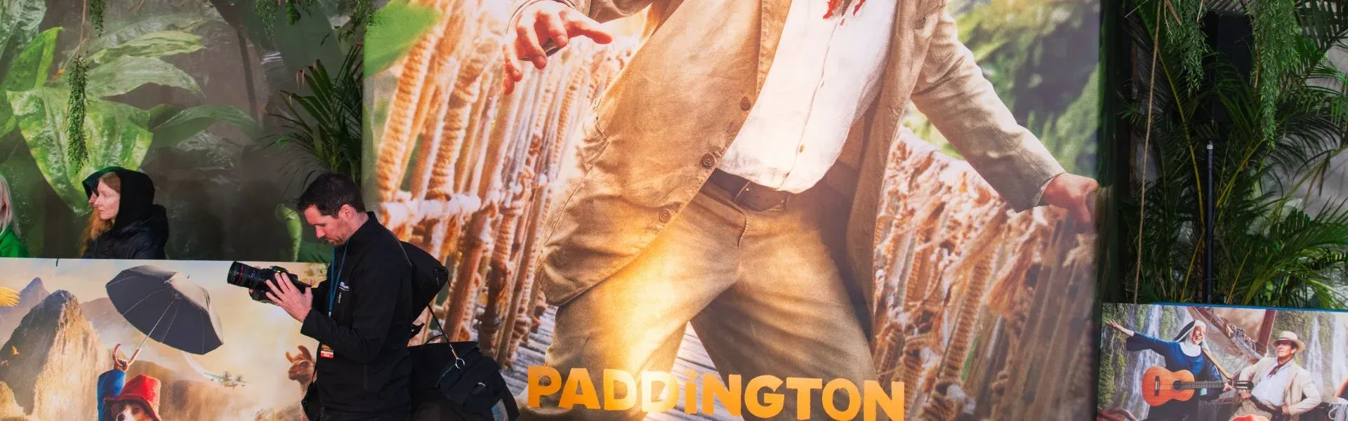 Large Paddington film poster: adventurer in a hat, jungle foliage. People in the foreground.