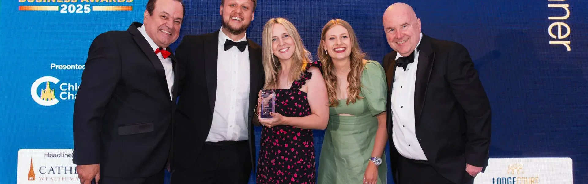 Five people, two women and three men, smiling on stage after winning 'Employer of the Year' award.