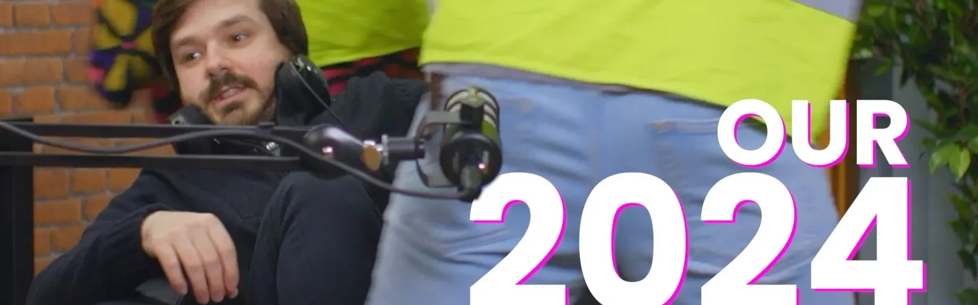 Man in black looks amused as person in high-vis walks past with camera rig.