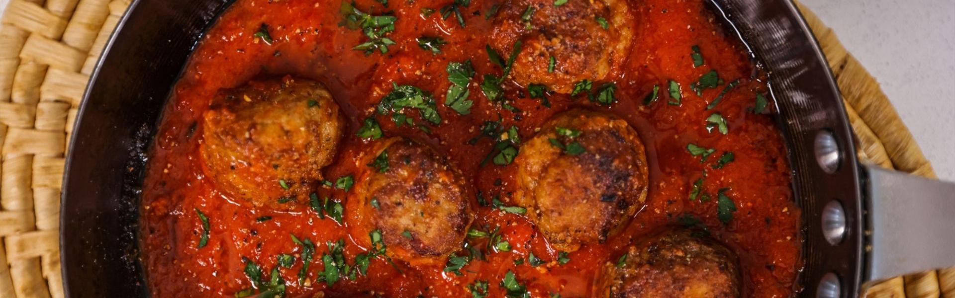 Meatballs in rich tomato sauce, garnished with fresh herbs, in a frying pan.