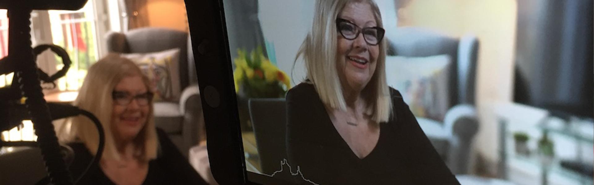Lady being interviewed on camera, shown sat at table and on camera monitor